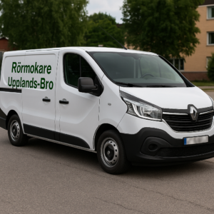 Vit Renault Trafic med texten "Rörmokare Upplands-Bro" på sidan, parkerad på en gata i Upplands-Bro. Registreringsskylten är blurrad.